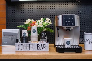 Angolo caffetteria con una macchina da caffè, bicchieri usa e getta e un cartello.