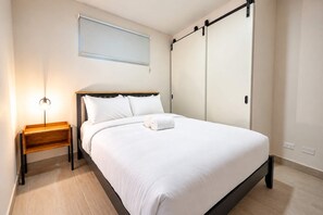 Ein Hotelzimmer mit Bett, Nachttisch, Lampe und einem Fenster mit Jalousien.