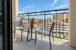 Ein Balkon mit zwei Stühlen und einem Tisch, einer Topfpflanze und Blick auf eine Stadtlandschaft.