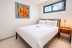 A bedroom with a bed, a nightstand, a wall-mounted artwork, and a window. - Apartment with Balcony (Panamá)