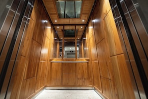 A modern elevator with wooden paneling and a glass ceiling, featuring a control panel and emergency exit. - Apartment with Balcony (Panamá)