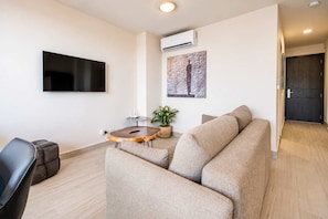 A modern living room with a flat-screen TV, a round wooden coffee table, a beige sofa, a potted plant, and a dark door in the background. - Apartment with Balcony (Panamá)
