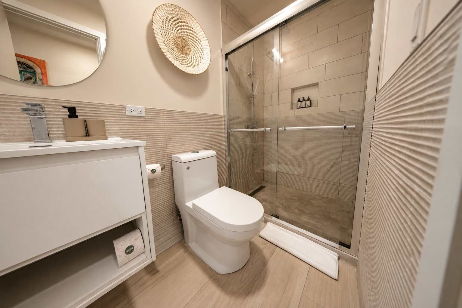 A modern bathroom with a toilet, a glass shower enclosure, and a vanity with a mirror.