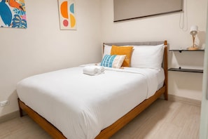 Una cama bien hecha con sábanas blancas, un cabecero de madera y una sola almohada.