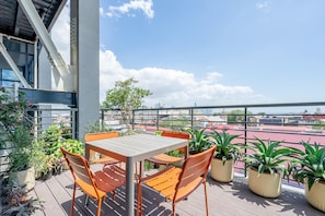 Terraza en la azotea con una mesa y sillas, rodeada de plantas en macetas, con vistas a un paisaje urbano.