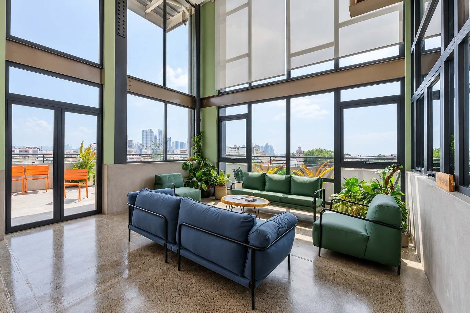 Una habitación amplia con ventanas grandes, un sofá verde, un sofá azul y una pequeña mesa.