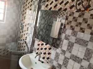 A bathroom with a glass shower enclosure, a sink, and a mirror. - 7 on Dutse Street Hotel (Abuja)
