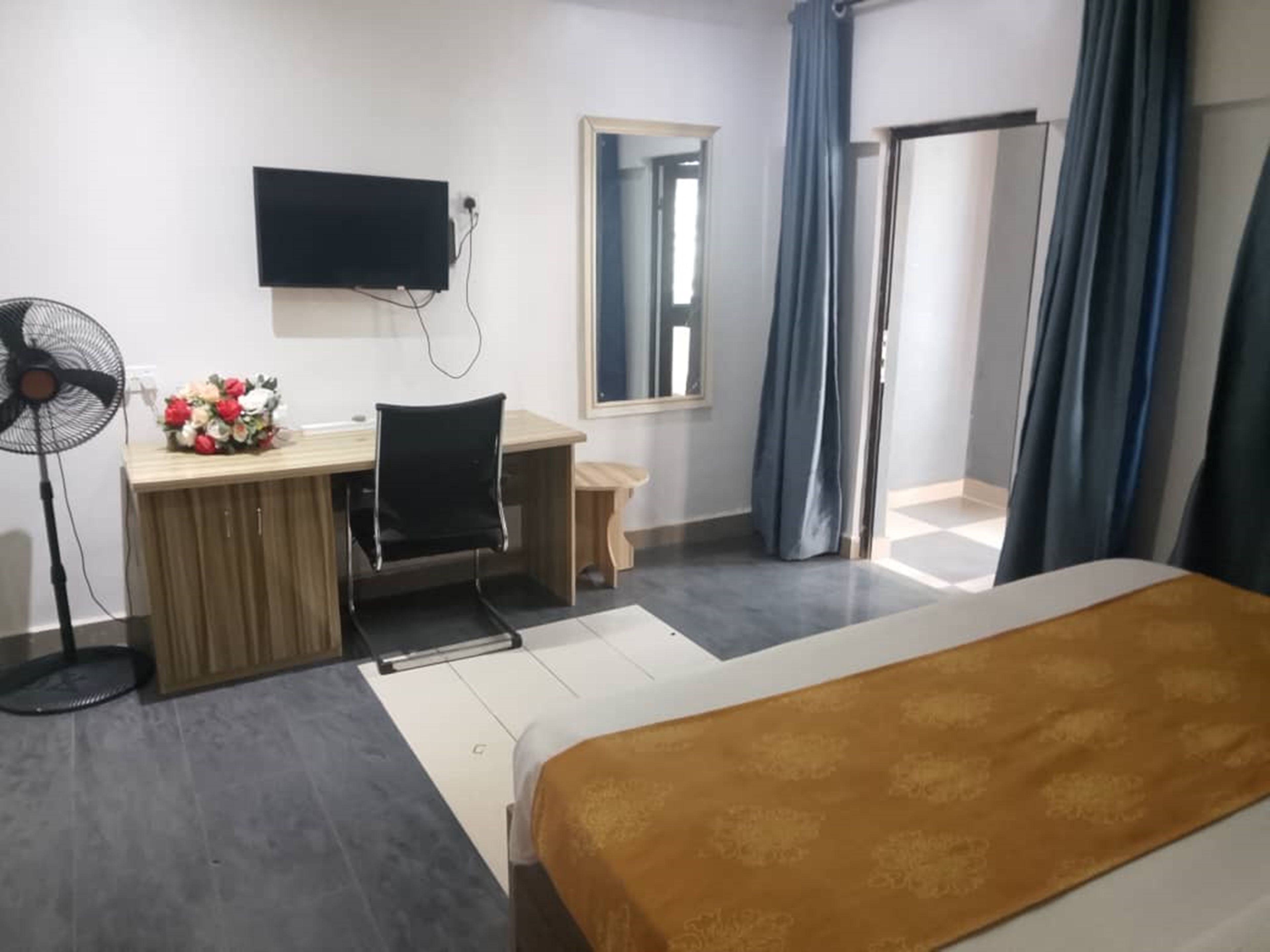 A hotel room with a bed, a desk, a chair, a TV, and a fan.