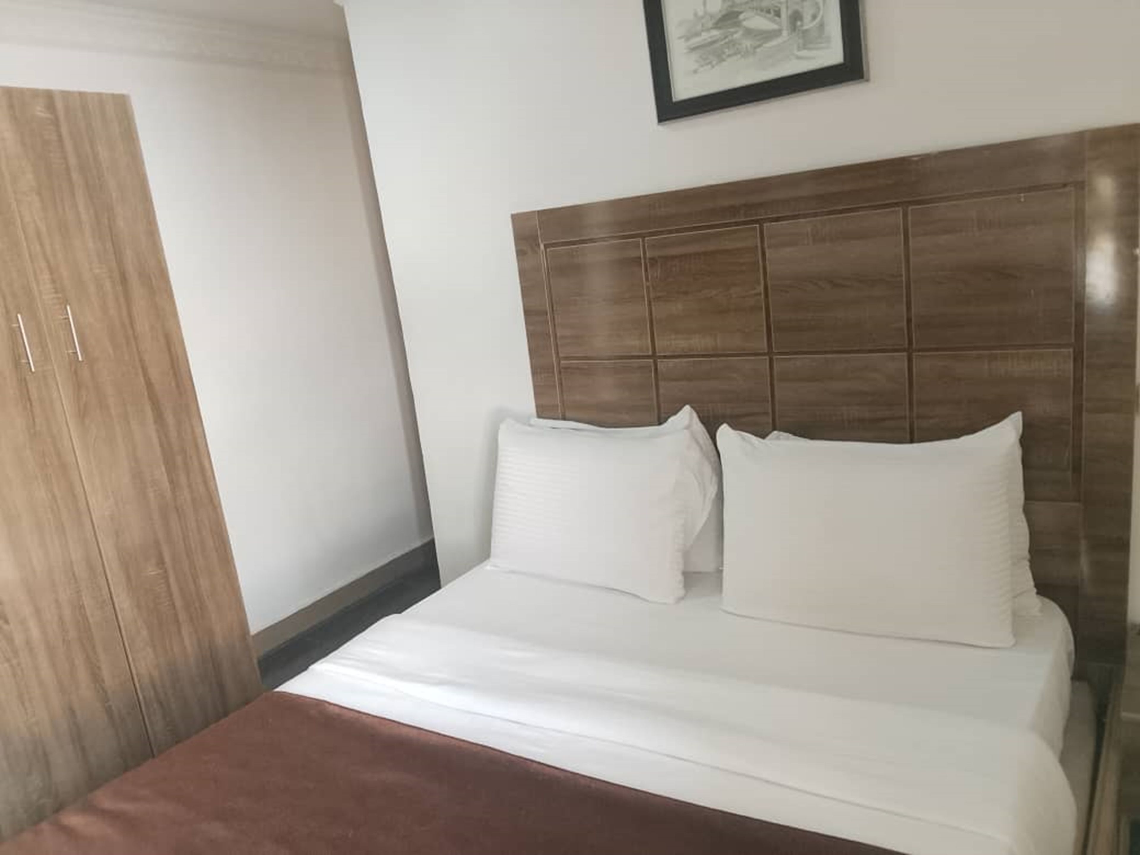 Habitació d'hotel amb un llit, un armari de fusta i un quadre al mur.