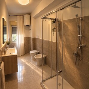 Un bany modern amb dutxa de vidre, vàter, bidet i rentapel.