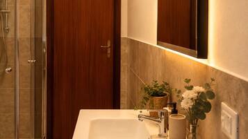 Ein Badezimmer mit weißem Waschbecken, einem Holflanschrank und einer Duschkabine aus Glas.