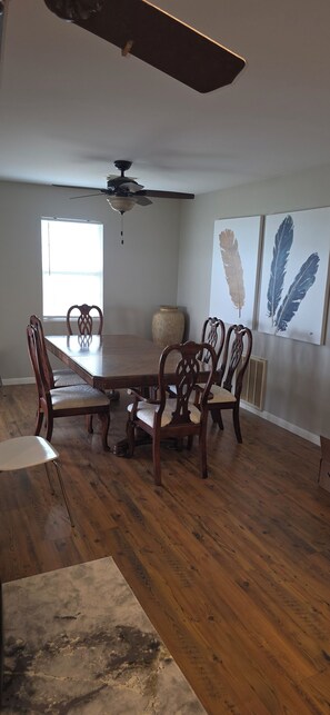 Un comedor con una mesa y sillas de madera, un ventilador de techo y decoración mural con plumas.