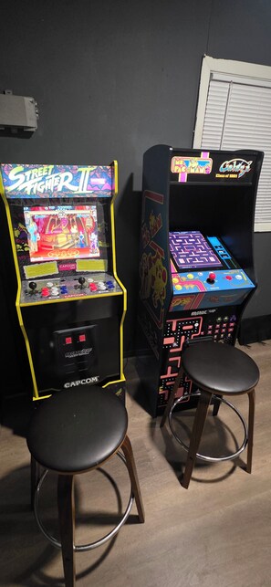 Two arcade machines with stools, one labeled 'Street Fighter II' and the other 'Pac-Man.'