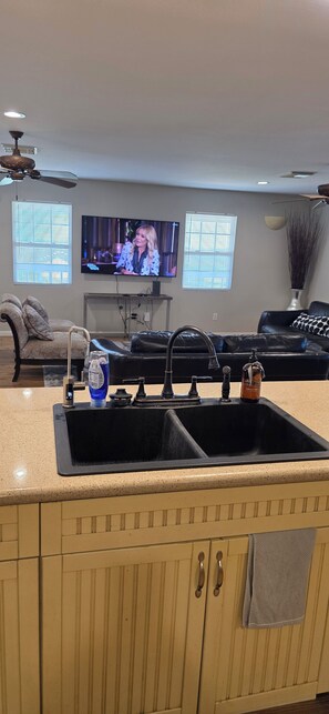 A kitchen with a double sink, a countertop, and a television in the background.