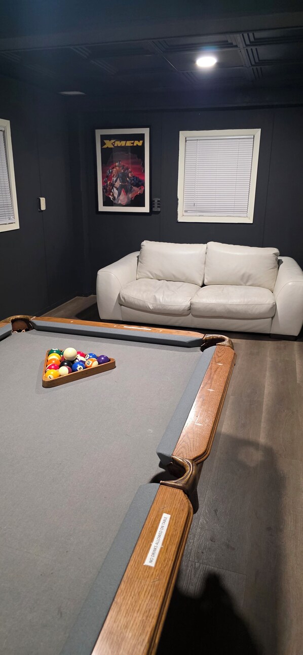 Una mesa de billar con bolas, un sofá de cuero blanco y un cartel en la pared.