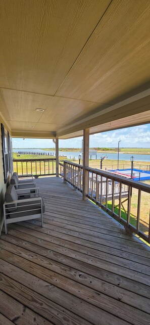 A covered outdoor deck with a view of a lake and a basketball court.