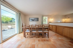 A dining area with a table and chairs, a painting on the wall, and a view through large windows. - Coin de paradis - Grande maison pour 14 pers (Saint-Philibert)