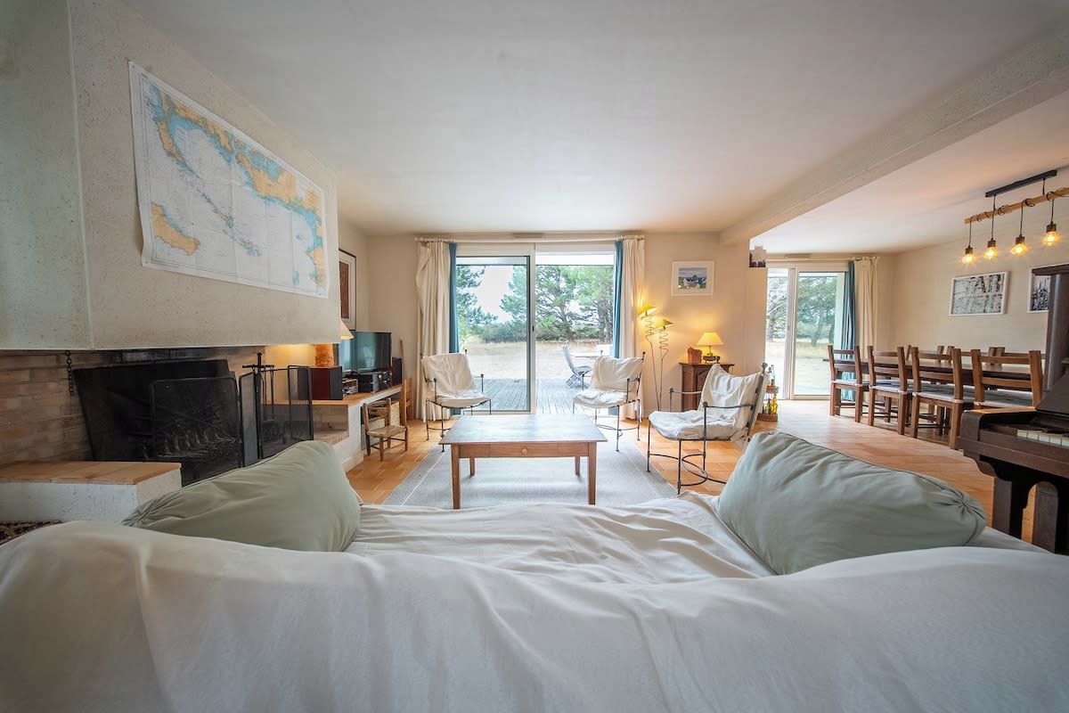Un salon spacieux avec un grand lit, une cheminée, un coin repas et une vue dégagée sur l’extérieur grâce aux portes vitrées.