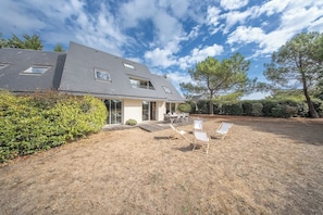 A modern house with a sloped roof, a covered patio with outdoor seating, and a well-maintained lawn. - Coin de paradis - Grande maison pour 14 pers (Saint-Philibert)