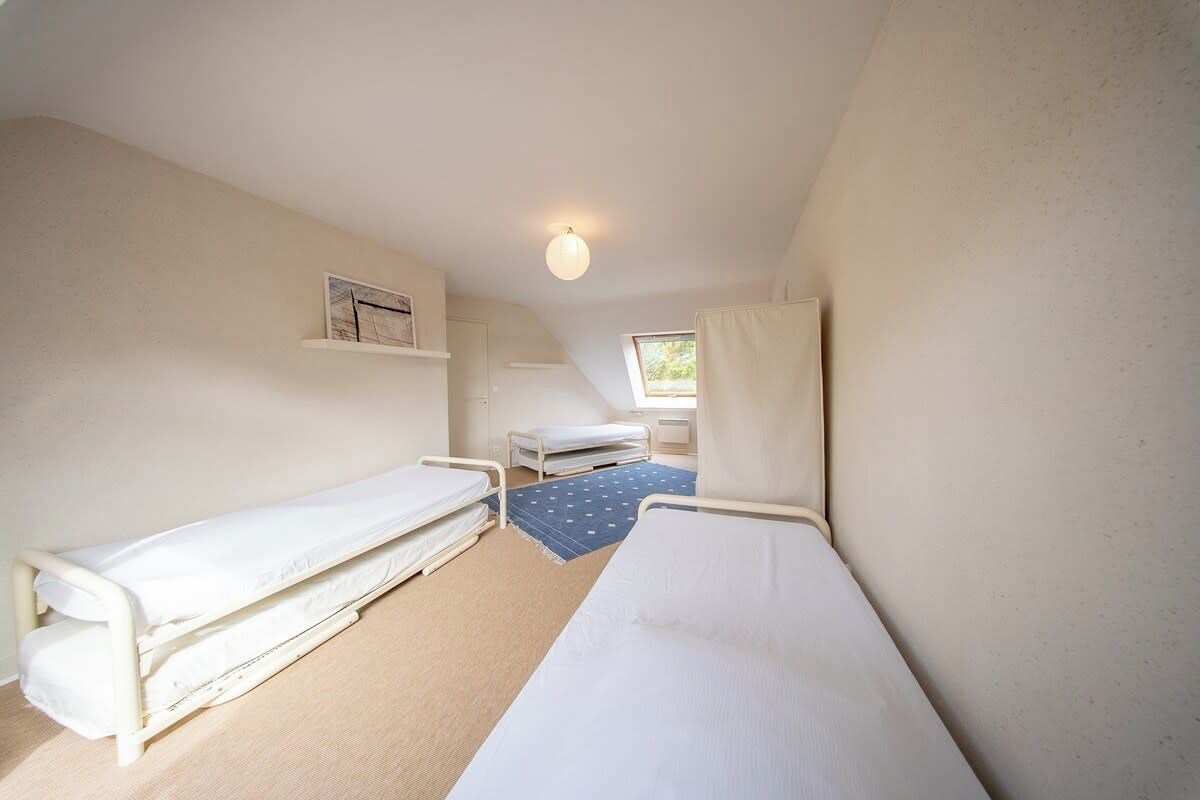 A small, single-room accommodation with two single beds, a window, and a light fixture.