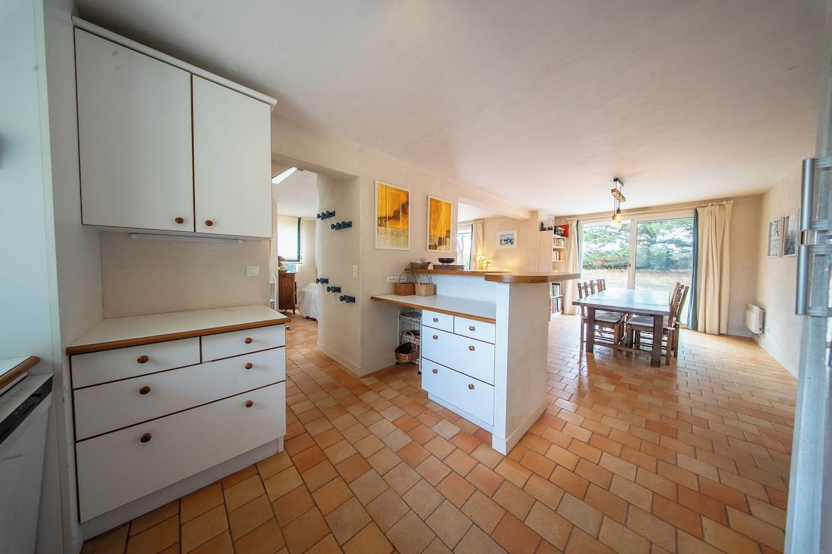 Een keuken met witte kastjes, een eettafel en een betegelde vloer.