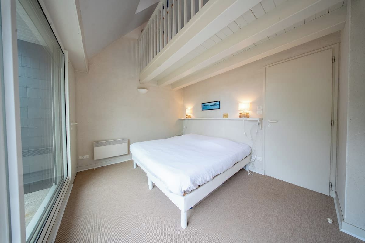 A bedroom with a bed, a radiator, a window, and a door.