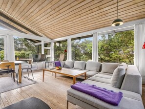 Ein modernes Wohnzimmer mit Holzboden, großen Fenstern, einer Couch, einem Couchtisch und einem Fernseher.
