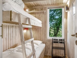 Ein Etagenbett mit einer Leiter, ein Fenster mit Blick auf Bäume und ein kleines Regal.