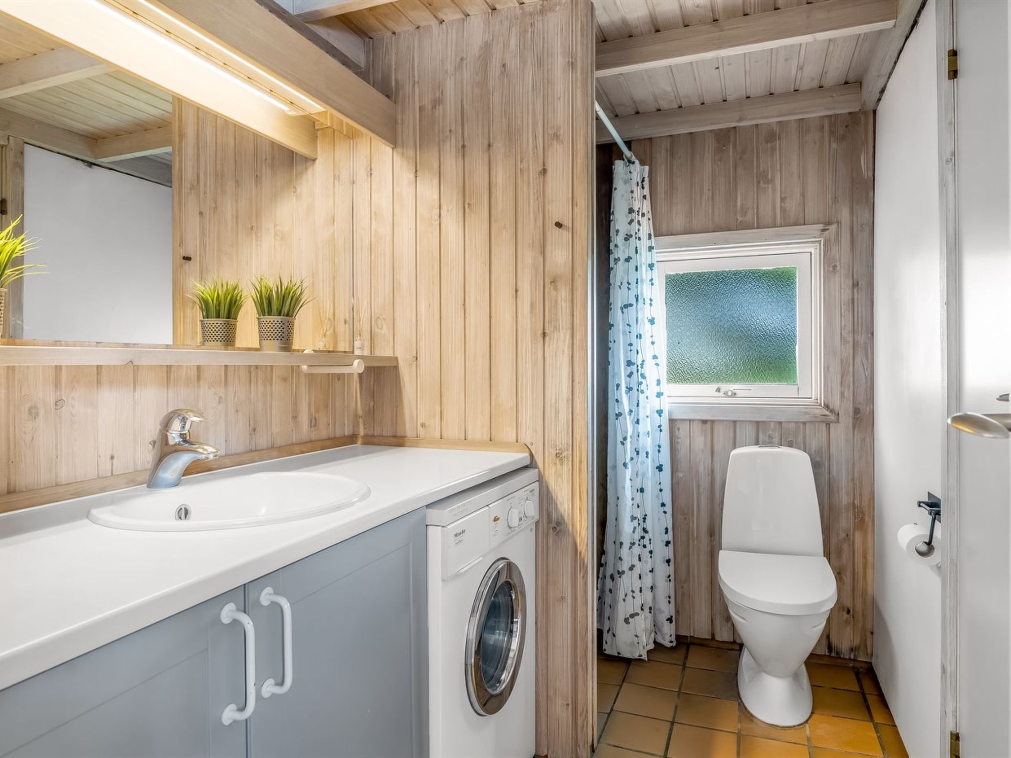 Un baño pequeño con lavabo, lavadora, inodoro y ventana con vistas.