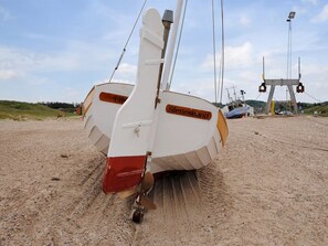 Ein Boot namens 'Slettesstrand' an einem sandigen Strand mit einer Krananlage im Hintergrund.