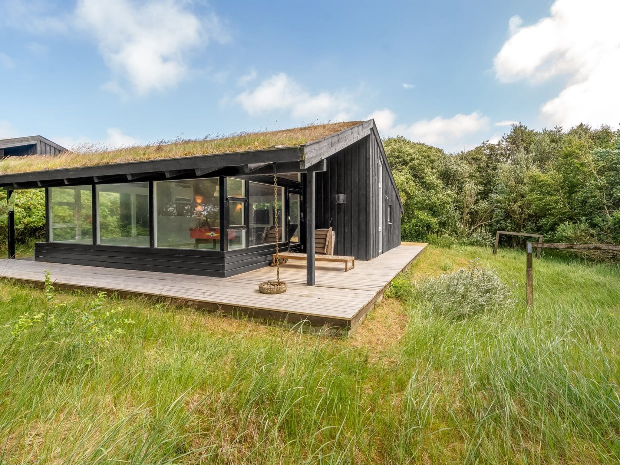 A modern house with a glass extension, a wooden deck, and a grassy field.