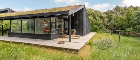 A modern house with a glass extension, a wooden deck, and a grassy field.