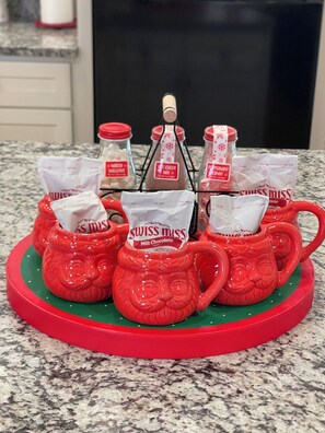 Uma bancada de cozinha com um tabuleiro decorativo vermelho contendo embalagens de chocolate quente Swiss Miss e uma garrafa de mistura para chocolate quente.