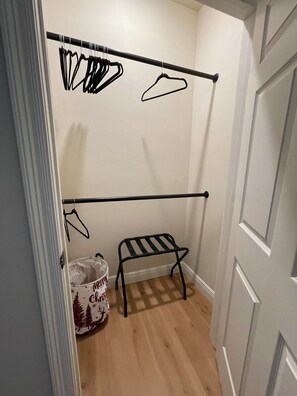 Ein Schrank mit zwei Kleiderstangen, einer Sitzbank und einer Tür mit weißem Rahmen.