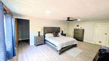 A bedroom with a bed, bedside tables, a ceiling fan, a nightstand, a dresser, and a door.