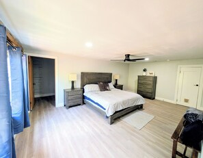Een slaapkamer met een bed, nachtkastjes, een plafondventilator, een dressoir en een deur.