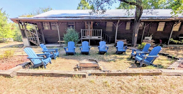Een rustieke blokhut met een veranda en meerdere Adirondack-stoelen in een halve cirkel gerangschikt.