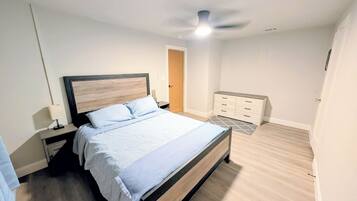 Een slaapkamer met een bed, nachtkastjes, een dressoir, een plafondventilator en een deur.