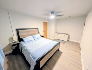 Un dormitorio con cama, mesitas de noche, cómoda, ventilador de techo y puerta.