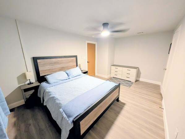 Un dormitorio con cama, mesitas de noche, cómoda, ventilador de techo y puerta.