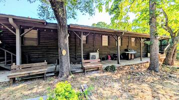 A rustic cabin with a covered porch, outdoor seating, and a grill area.