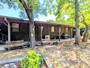 Een rustieke houten hut met een overdekte veranda, buitenmeubels en een barbecueplaats.