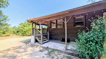 A wooden cabin with a porch, a set of stairs, and a gravel driveway.