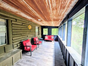 Une cabane en rondins dotée d’un porche couvert, de sièges rembourrés de couleur rouge et d’une grande fenêtre donnant sur un paysage verdoyant.