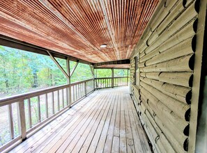 Une terrasse en bois surmontée d’un toit en métal, entourée d’arbres.