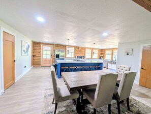 Een ruime keuken met een centraal eiland, houten kastjes en een eethoek met een tafel en stoelen.