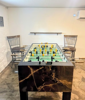 A foosball table in a room with two chairs and a wall-mounted air conditioning unit. - The Hilltop Farmhouse (Mena)