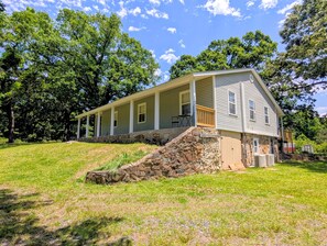 A two-story house with a porch, stone steps, and a small shed in a grassy area. - The Hilltop Farmhouse (Mena)