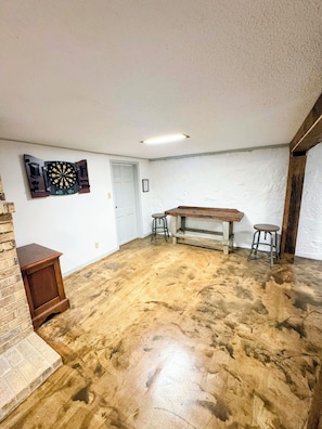 A room with a wooden bench, two stools, a dartboard, and a door. - The Hilltop Farmhouse (Mena)