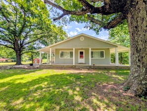 A single-story house with a porch, surrounded by grass and trees. - The Hilltop Farmhouse (Mena)
